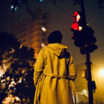 赤信号の下で立ち止まって信号待ちをする人物の後ろ姿