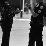 警察官が路上で市民に職務質問し同行を求めている様子