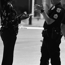 警察官が路上で市民に職務質問し同行を求めている様子