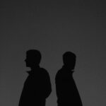 検面調書と公判供述の相反を表す背中合わせの人物イメージ